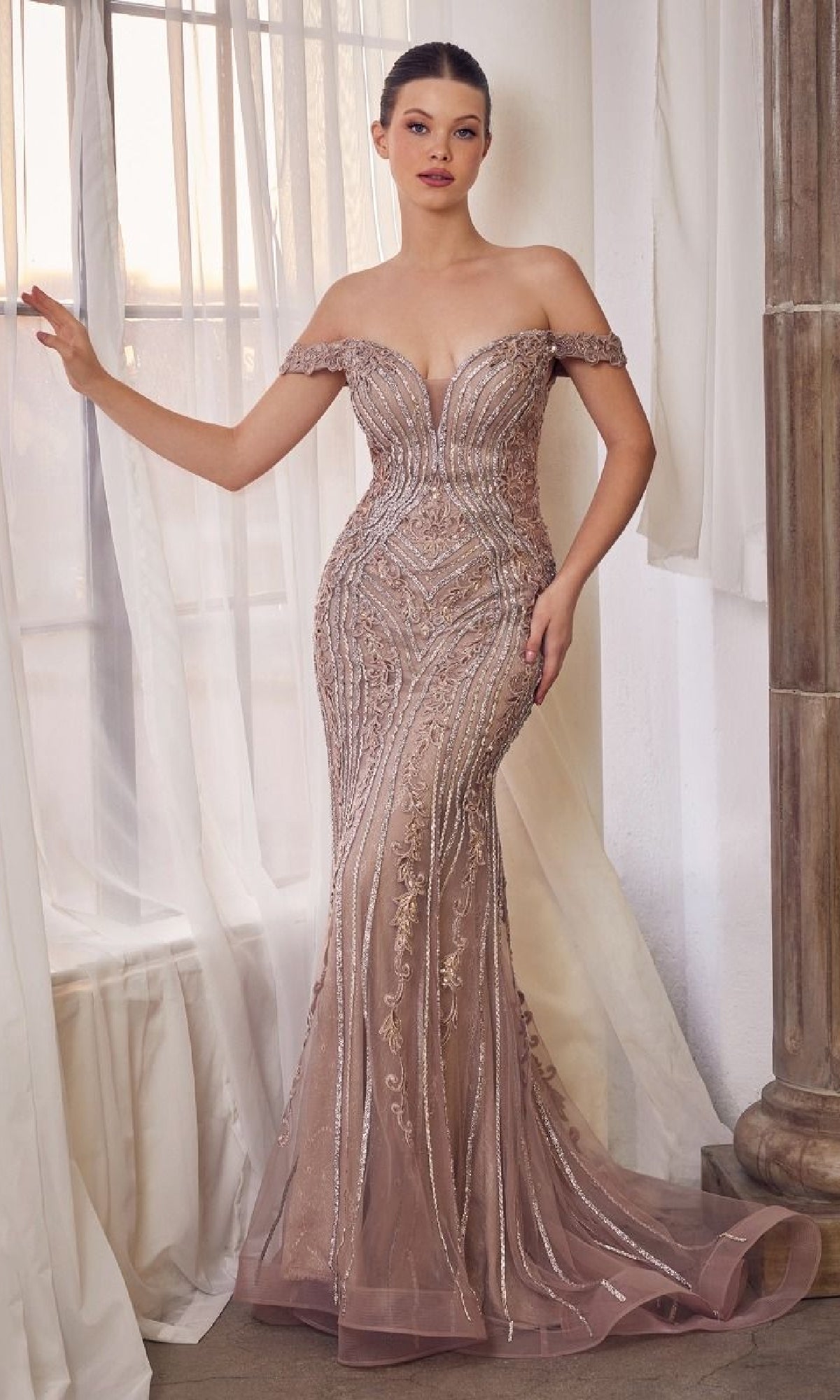 A woman stands by a window in the Andrea & Leo A1257 mauve pink long prom dress, featuring off-the-shoulder design and intricate beadwork for an elegant, stunning look.